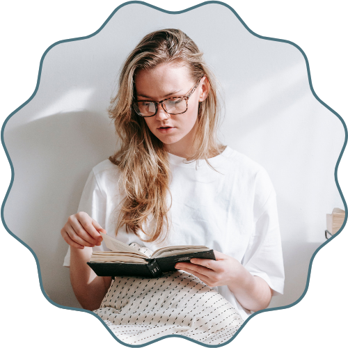 A young person sitting in a cozy chair, reading a hardcover book.